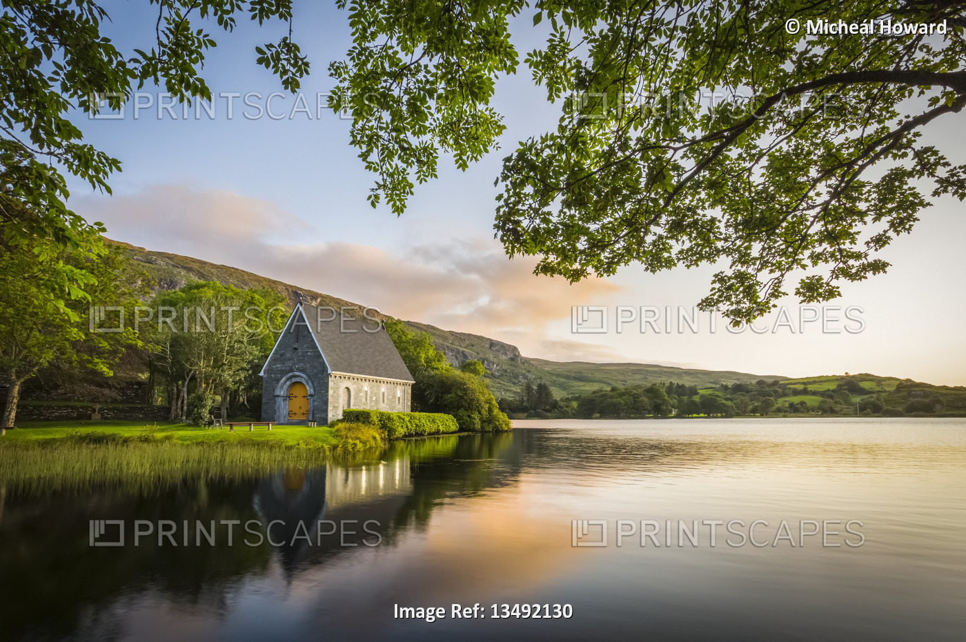 Old chapel of Gougane Barra situated by a lake and framed by green trees at ...